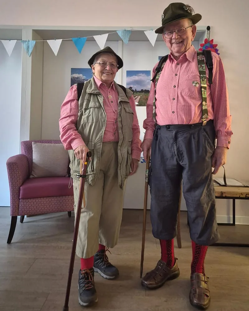 Hier sehen Sie zwei verkleidete Tagesgäste aus der Tagespflege SCHÖNES LEBEN Gotha am Neumarkt in traditionellen Oktoberfest-Trachten mit Lederhosen, Wanderstock und Hut.